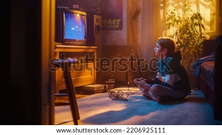 Nostalgic Childhood Concept: Young Boy Playing an Old-School Arcade Video Game on a Retro TV Set at Home in a Room with Period-Correct Interior. Kid Waiting For Level to Load. Royalty-Free Stock Photo #2206925111