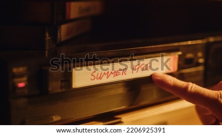Close Up of a Person Inserting a VHS Cassette in a Player with Nostalgic Summer Footage from Home Video Camera. Retro Nineties Technology Concept. Old VCR with Shallow Depth of Field and Bokeh. Royalty-Free Stock Photo #2206925391