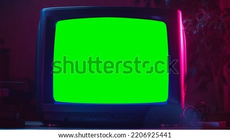 Close Up Footage of a Dated TV Set with Green Screen Mock Up Chroma Key Template Display. Nostalgic Retro Nineties Technology Concept. Vintage Television Display in Neon Lit Living Room.