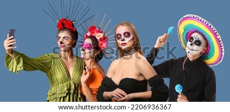 Young people with skulls painted on faces against blue background. Celebration of Mexico's Day of the Dead (El Dia de Muertos)