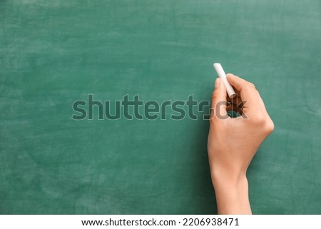 Female hand with chalk against green blackboard