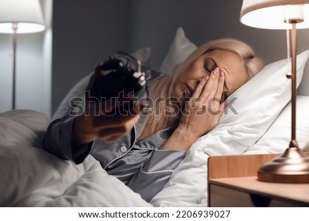Stressed mature woman with alarm clock lying in bed at night Royalty-Free Stock Photo #2206939027