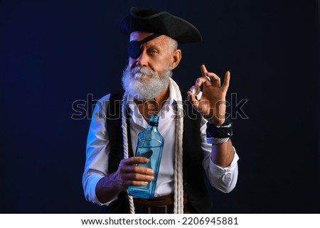 Old pirate with bottle of rum on dark background