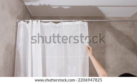 A man opens a shower curtain in the bathroom to protect against splashing water. Modern bathroom, hygienic Royalty-Free Stock Photo #2206947825