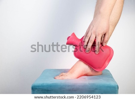 Treatment of arthritis of the ankle joint with a heating pad with hot water. Royalty-Free Stock Photo #2206954123
