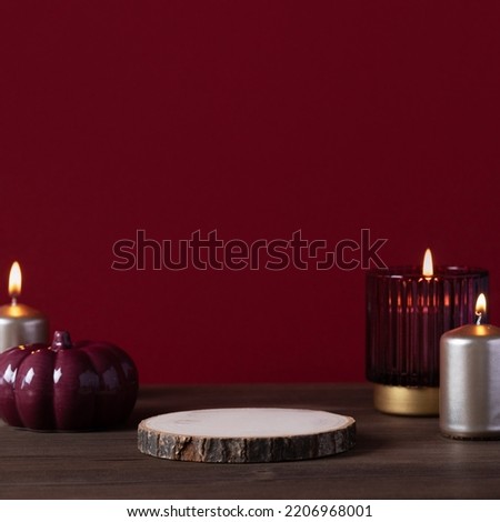 Empty wooden podium on wooden table with ceramic pumpkin decor and golden candles on dark burgundy color background. Autumn product podium still life
