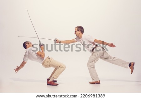 Portrait of two men in a suit fighting with swords isolated over grey studio background. Dynamic image. Concept of sport, hobby, emotions, active lifestyle, retro fashion. Copy space for ad Royalty-Free Stock Photo #2206981389