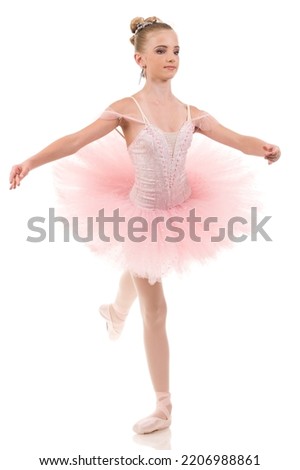 Young woman ballerina in white tutu, dancing on pointe with arms overhead, in the studio against a dark background. High quality photo
