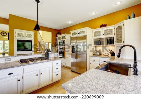 Farm house interior. Luxury kitchen room in bright yellow color with white cabinets, steel appliances and granite