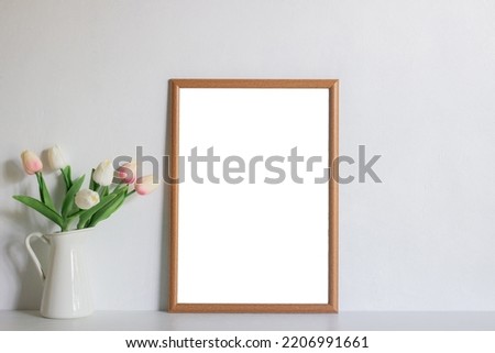 A wooden photo frame and tulips on white wall with natural light. 