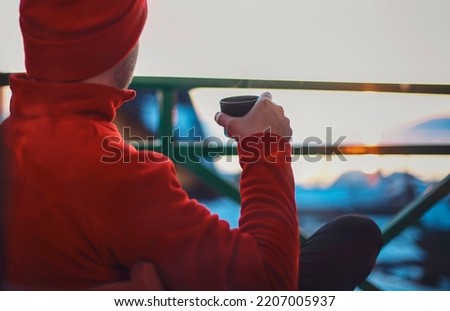 Man in winter clothing drinking hot herbal tea. Winter evening from a beautiful balcony in the suset time on Baikal Lake. Winter tourism