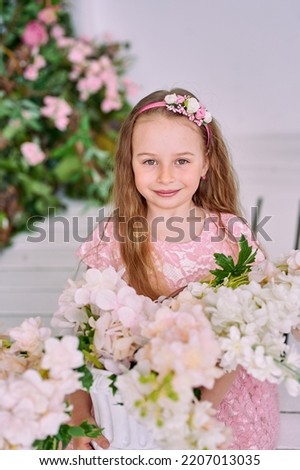 a little girl with beautiful hair and a round face sitting in white flowers. Girl with hoop and smiling beautifully. High quality photo