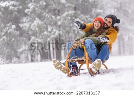 Beautiful young couple in love having fun spending winter vacation in mountains, sitting and hugging on sled, sliding down the hill in the snow Royalty-Free Stock Photo #2207013157