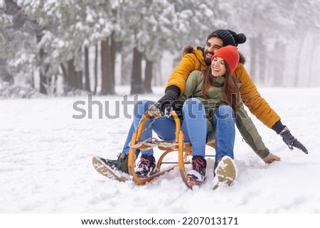 Beautiful young couple in love having fun sledging while spending winter vacation in mountains