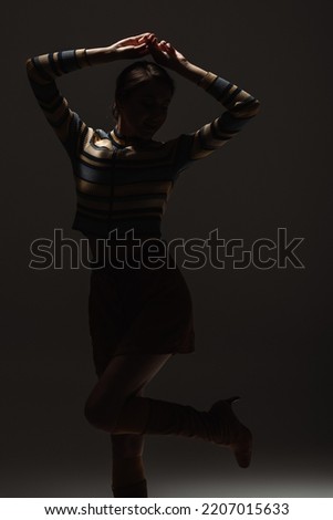 silhouette of young woman in autumnal stylish outfit posing on black