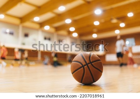 Basketball Training Game Background. Basketball on Wooden Court Floor Close Up with Blurred Players Playing Basketball Game in the Background
