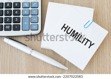 Humility text on the card on a clip on a wooden background next to the pen and calculator