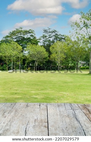 Empty wooden table-top in natural green park With lawn background and large outdoor trees in the daytime in Thailand, simulated for displaying edited products or designing layouts.
