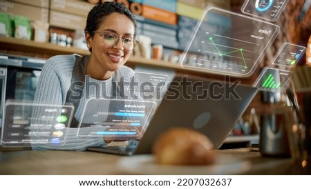 Beautiful Latina Coffee Shop Owner is Working on Laptop Computer and Checking Inventory in Cozy Cafe. Restaurant Manager Browsing Internet and Chatting with Friends. VFX Augmented Reality Concept. Royalty-Free Stock Photo #2207032637