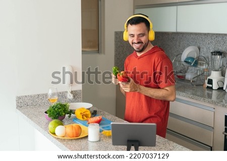 Young man cooking lunch while doing a video chat with his tablet at modern kitchen