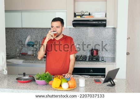 man sips a beer while preparing a meal in his home kitchen