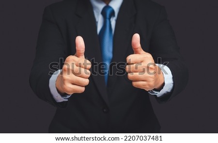 A businessman in a suit shows thumbs up with both hands while standing on gray background. Customer service and satisfaction surveys concept. Close-up photo