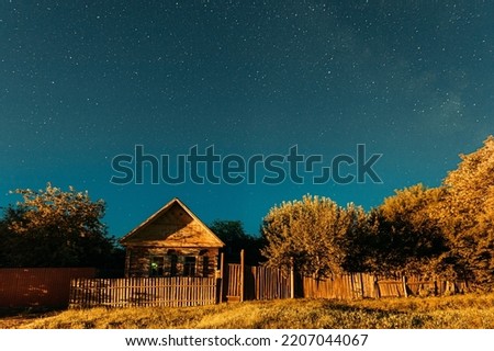 Night sky over house in old village. Night starry sky above house with bright stars and meteoric track trail. Glowing stars above summer nature.