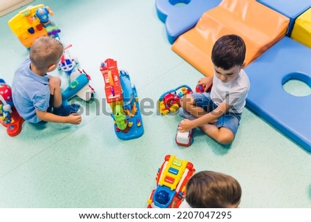 Toddlers boys and their nursery teacher playing with plastic toys and colorful car in a nursery school playroom. Imagination and Creativity. Cognitive Growth. High quality photo