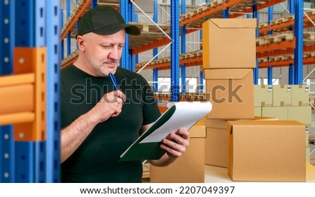 Storekeeper making revision. Man storekeeper in front of cardboard boxes. Warehouse worker thought. Guy with pen next to warehouse racks. Storekeeper man takes care of incoming goods Royalty-Free Stock Photo #2207049397