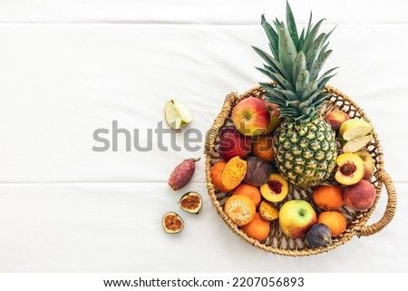 Pineapple and other exotic fruits in a basket on a white background, top view.