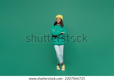 Full body happy little kid teen girl of African American ethnicity 13-14 years old wear casual hoody hat hold hands crossed folded look camera isolated on plain dark green background Childhood concept Royalty-Free Stock Photo #2207066725