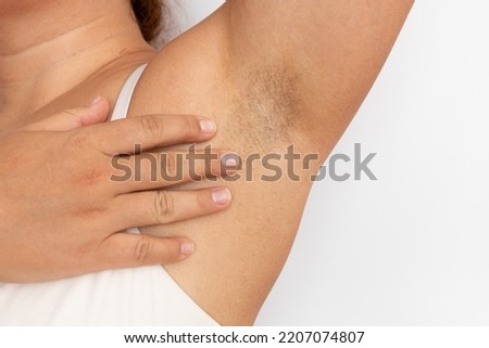 Woman touch hairy underarms with hand closeup, free copy space, beige background. Raised arm with armpit hair. Female beauty trend, freedom, feminism, body positive, naturalness. Hygiene concept.
