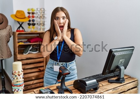 Young brunette woman holding banner with open text at retail shop afraid and shocked, surprise and amazed expression with hands on face 