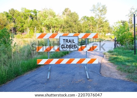 Trail closed warning sign with white and orange stripes along walking path in urban hiking zone landscape photo. 
