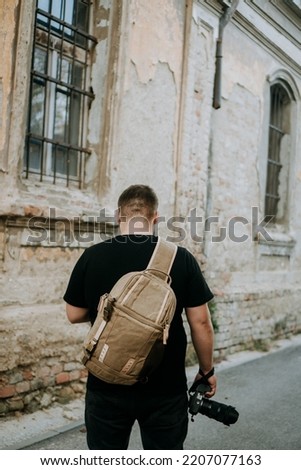A man with a brown camera bag and a camera in hand walking around an old town