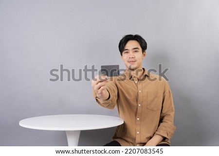 A photo of a happy, positive, handsome Asian man showing a club card or credit card to the camera