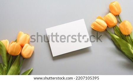 white blank card, yellow tulip flower on grey background , top view
