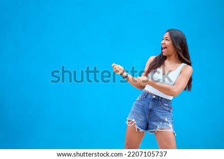 Happy isolated copy space shot with an African American young lady pulling an invisible sign for promotions, face expression, open mouth, blue background to fill up with information.