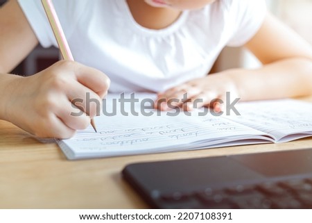 A kid is practicing and writing English cursive handwriting words in a notebook with online learning. Cursive handwriting practice. Pencil grasp activities. Kindergarten skills. Focus on pencil tip. Royalty-Free Stock Photo #2207108391