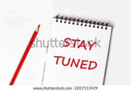 Red pencil and white notepad with the text STAY TUNED Royalty-Free Stock Photo #2207113439