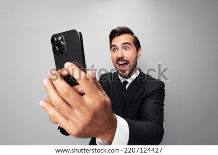 Man businessman holding phone in hand surprised looking at screen video call and selfies and smile with teeth. Close-up wide angle photo gray isolated background