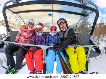 Family riding ski lift cable car on winter vacation skiing. Family on winter vacations ski trip taking selfie on ski lift with amazing mountain view of the ski resort and slopes. Active Family