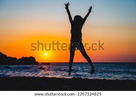 Silhouette of a child jumping in sunset on a beach. Little girl jumping with hands raised on a sunset beach with the sea in the background. Amazing sunset in Sfinari beach, Crete, Greece.
