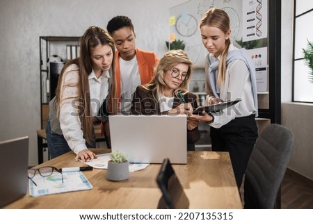 Teamwork, brainstorming in office. Diverse multiracial business people working together with laptop and tablet pc while their senior woman leader sign in report papers.