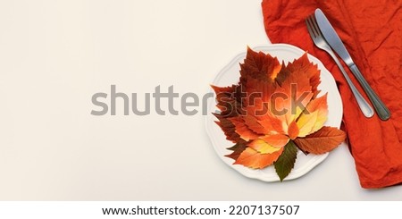 Autumn table setting, above view plate decorated red leaves and cutlery on red napkin on beige background, banner with copy space. Aesthetic autumn home and table decor. Fall holiday natural decor.