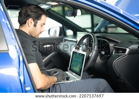 Mechanic AsianArab man using laptop computer examining tuning fixing repairing car engine automobile vehicle parts using tools equipment in workshop garage support service in overall work uniform Royalty-Free Stock Photo #2207137697