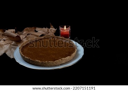 Homemade pumpkin pie on black background with fall leaf and candle