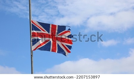 frayed English flag at half mast all ruined due to bad weather Royalty-Free Stock Photo #2207153897