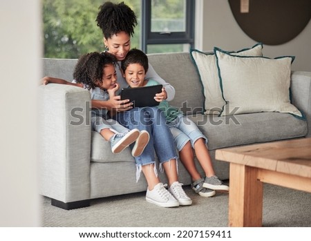 A mother with children on couch with tablet to watch educational shows and streaming music. Foster or adoption parent with kids in living room watch cartoons, playing online games and homeschooling.