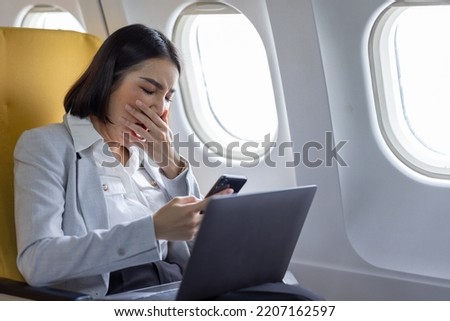 Traveling and technology. Flying at first class. Pretty young Asian business woman using smartphone while sitting in airplane.